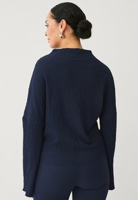 Marineblå struktureret sweater med en løs pasform, rund halsudskæring og brede ærmer. Har et subtilt krøllemønster og ribbet kant.