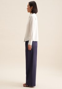 Weiß gestreiftes Langarmhemd mit Kragen, kombiniert mit hochtaillierten navyblauen Palazzo-Hosen und getragen mit schwarzen Riemchensandalen.