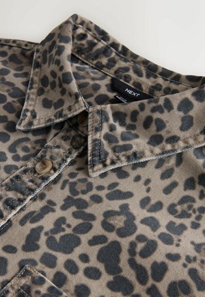 Leopard print shirt featuring a tan background with black spots, button closure, and a folded collar. Material appears textured, likely cotton.