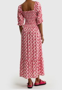 Kukallinen mekko, jossa on neliön muotoinen kaula-aukko, lyhyet puffihihat ja smokkatussa yläosassa. Vaaleanpunainen ja valkoinen kangas punaisilla ruusukuvioilla; kerroksellinen hame.