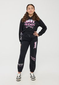 Set di felpa nera con cappuccio e pantaloni felpati caratterizzato da colorate grafiche "MIGLIORI AMICI". Il tessuto è morbido, con polsini elastici e vita con cordino.
