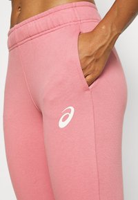 Rosa Sportleggings aus weichem Material mit einem elastischen Bund und einer Seitentasche, versehen mit einem weißen Logo-Akzent auf dem Oberschenkel.