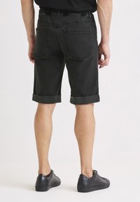 Svarta denimshorts med uppvikta fållar, resår i midjan och bakfickor. Mjuk yta, avslappnad passform, bärs med svarta sneakers.