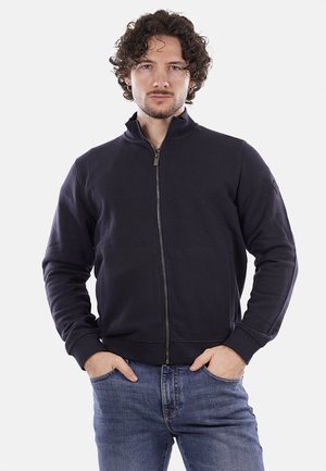 Felpa con zip color navy, collo alto, texture morbida, polsini e vita a costine; dotata di tasche laterali e logo del brand discreto sulla manica.