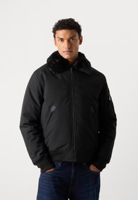 Black bomber jacket with a faux fur collar, zip closure, and side pockets. Features elastic cuffs and a sleek, textured finish.