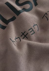 Tessuto rosa chiaro con una superficie texturizzata, caratterizzato da testo e simboli stampati in nero, con pieghe e ombre visibili.