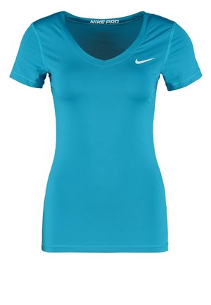 Femme portant un t-shirt de sport bleu vif, un short bleu foncé avec des accents bleu clair, et des baskets blanches avec des lacets jaune néon, debout droite.