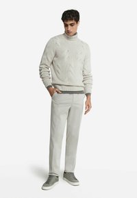 Ljust grått stickat turtleneck-tröja med ett texturerat mönster, kombinerat med ljusgrå byxor och grå sneakers. Avslappnad passform och modern design.