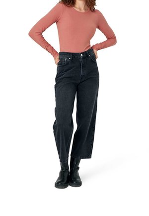 Zwarte jeans met hoge taille en wijde pijpen, voorzien van vijf zakken en zilverkleurige details. Gecombineerd met een geribd roestkleurig topje met lange mouwen en zwarte laarzen.