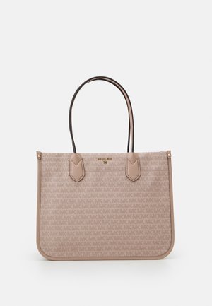 Beżowa torba typu tote Michael Kors z tkaniną z wzorem logo, dwoma wąskimi paskami na ramię i złotą plakietką z logo na środku przodu.