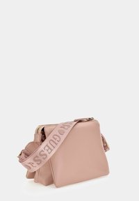 Vaaleanpunainen keinonahkainen olkalaukku, jossa vetoketjukiinnitys ja leveä hihna, johon on painettu kontrastivärinen "GUESS"-teksti. Kompakti ja muotoiltu design.