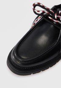 Zwarte leren schoen met een ronde neus, voorzien van een gestructureerde afwerking en contrasterende geruite veters in rood en wit. Dikke rubberen zool.