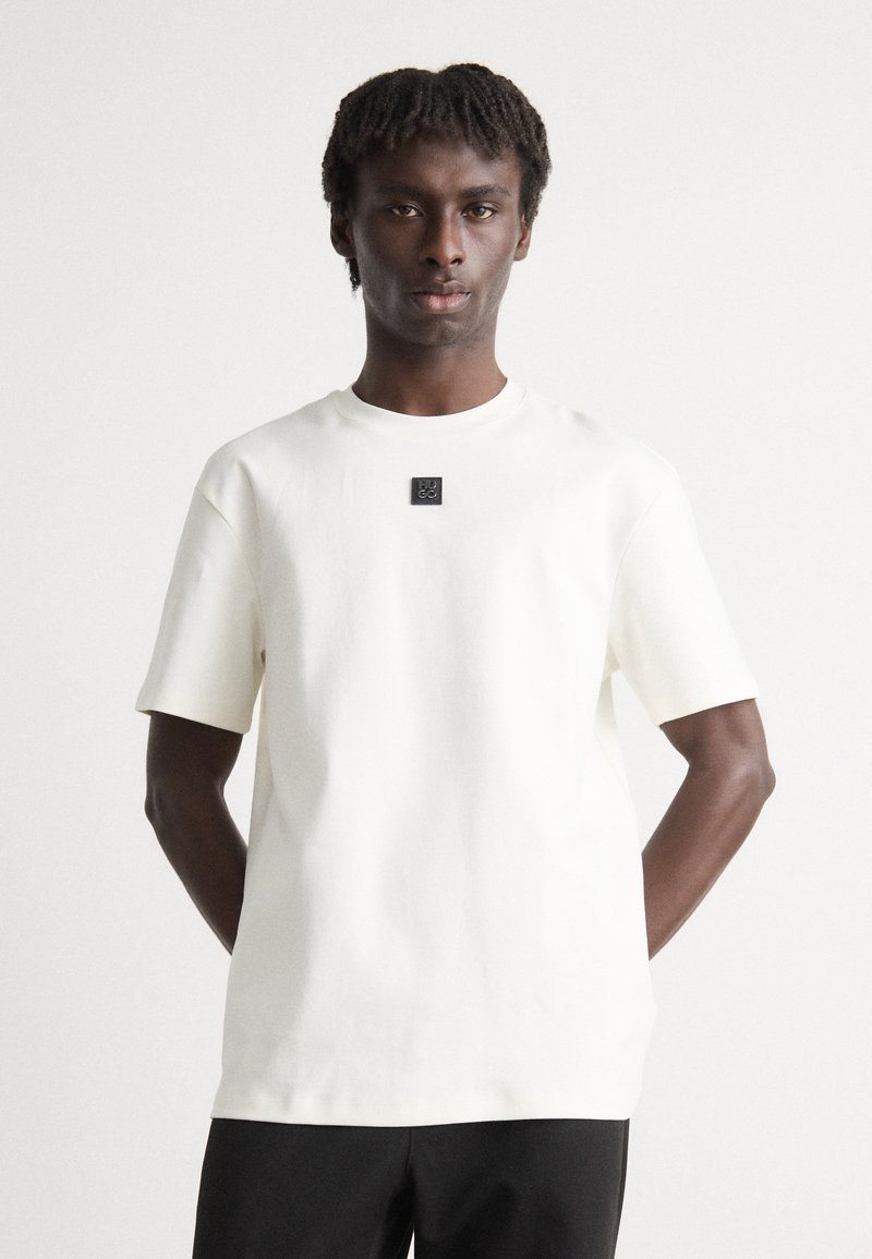 Weiße Kurzarm-T-Shirts aus weichem Material, mit einem schwarzen quadratischen Etikett auf der Brust. Gerader Schnitt, schlichtes und minimalistisches Design.