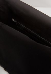 Interno di una borsa in tessuto nero con texture liscia, dotato di un compartimento con zip per una conservazione sicura. Design semplice e minimalista.