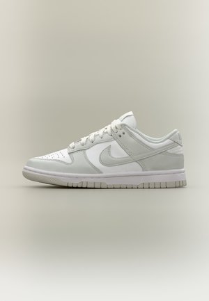 Basket Nike blanche à tige basse, avec bout perforé, laçage sur le devant, logo Swoosh et semelle en caoutchouc texturée sur un fond uni.