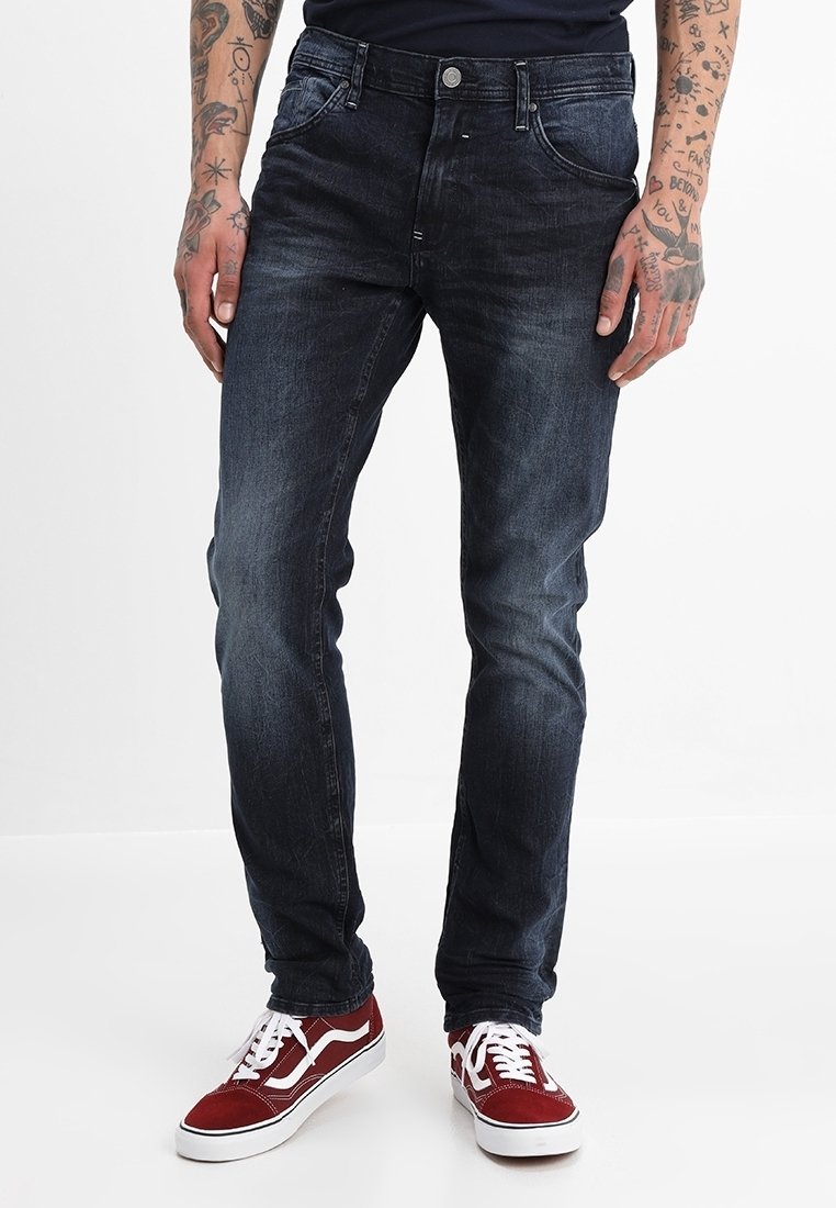 Mörkblå jeans i denim med normal passform, fem fickor, gylf med knappar och subtila slitage-mönster, tillsammans med röda och vita sneakers.
