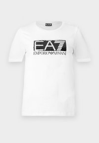 Λευκό κοντομάνικο T-shirt με μαύρο και λευκό παγιετένιο λογότυπο "EA7" και το κείμενο "Emporio Armani" κάτω από το στήθος.