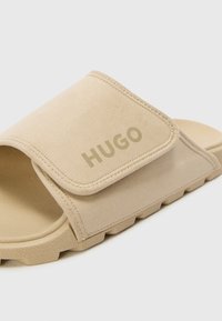 Beige sky sandal med semsket overdel, justerbar stropp med "HUGO"-logo og teksturert gummisåle med riller for godt grep.