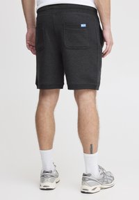 Shorts en coton gris foncé avec une taille côtelée et deux poches arrière. Comprend une petite étiquette bleue sur la taille. Design athlétique décontracté.