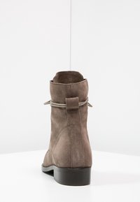 Braune Wildleder-Ankle Boots mit runder Zehenpartie, niedrigem Absatz und dekorativem Bindedetail an der Rückseite. Glatte Textur und minimalistisches Design.