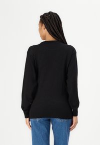 Black knitted sweater with long sleeves, ribbed cuffs and hem, plain design, paired with blue denim jeans.