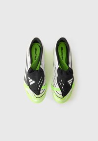 Sorte og hvite fotballsko med teksturert overdel, grønne detaljer, slip-on design og gummisåle med rutenettmønster.