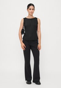 Top sans manches plissé noir avec un col rond, accompagné d'un pantalon noir ajusté. Les accessoires comprennent un petit sac à main noir et des chaussures à plateforme.
