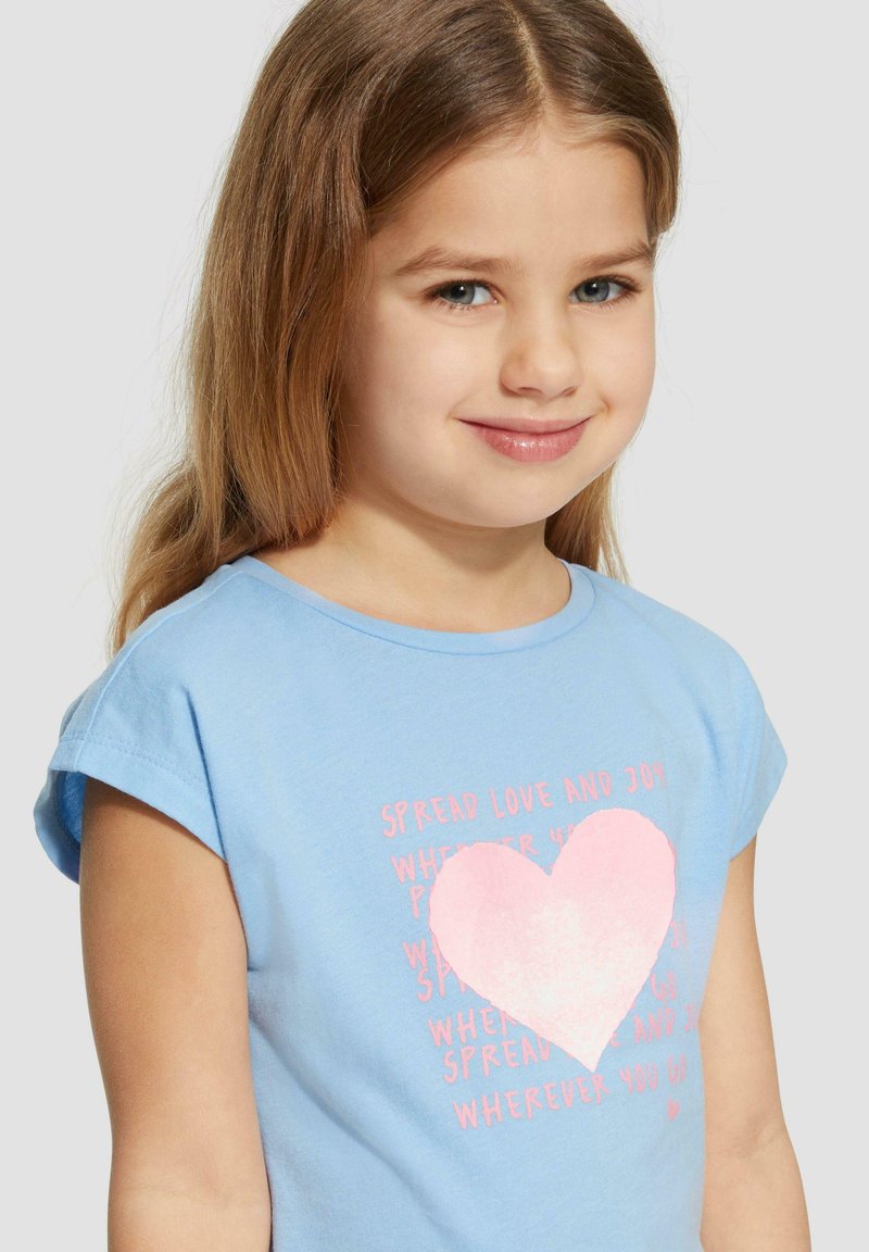 Lichtblauwe katoenen T-shirt met korte mouwen, met een grote roze hartafbeelding en roze tekst "Verspreid liefde en vreugde" op de voorkant.