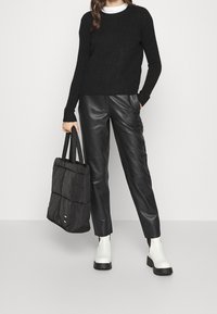 Svart stickad tröja, svarta läderbyxor, vita ankelskor och en svart vadderad tote-väska med remmar. Fokusera på textur och monokrom stil.