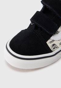 Μαύρο σουέντ αθλητικό παπούτσι με λουριά Velcro, λευκή λαστιχένια σόλα και τυπωμένο ύφασμα με γραφικό σχέδιο στο πλάι.