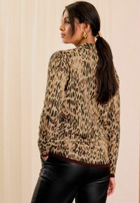 Pulover s leopard uzorkom u bež i smeđoj boji, uskog kroja, rebrasti donji rub s burgundi detaljima, kombiniran s crnim hlačama od umjetne kože.