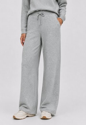Person iført lysegrå vidde joggingbukser med snøre i taljen, matchende lysegrå sweater og off-white sneakers med gumssåler.