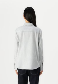 Camicia a maniche lunghe a righe in cotone azzurro chiaro e bianco, con colletto, orlo curvo e polsini con bottoni, indossata con jeans scuri.