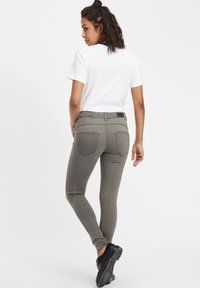 Jeans skinny elásticos grises con cintura alta, diseño de cinco bolsillos y una etiqueta con logo negra en la parte de atrás, combinados con una camiseta blanca básica.
