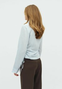 Haut texturé bleu clair à manches longues et liens sur le côté, associé à un pantalon taillé marron foncé. La chemise présente des rayures verticales.