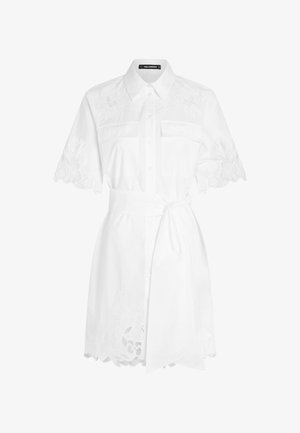 Vit skjortklänning med krage, korta broderade ärmar, två bröstfickor och midja med bälte. Spetsdetaljer vid fållen.