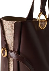 Braune Leder-Tote mit einem Akzent aus leicht strukturiertem Stoff, ausgestattet mit goldfarbenen Beschlägen und einem kreisförmigen Ringdetail. Glatte Oberfläche und robustes Design.
