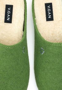 Green felt slip-on slippers with a beige lining and embroidered logo detail. Rounded shape with a soft texture, suitable for indoor wear.