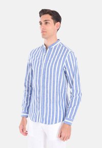 Camicia a righe blu e bianche con colletto alla cinese, maniche lunghe e tessuto leggero. Presenta strisce verticali strette.