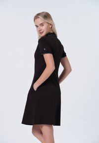 Robe polo noire à manches courtes, en tissu texturé, avec poches et finitions contrastantes au col et aux bords des manches.