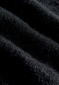 Zbliżenie na miękką, czarną tkaninę wełnianą, ukazującą drobne włókna i teksturowane fałdy w słabym świetle.