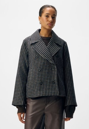 Double-breasted jacket in navy and cream houndstooth pattern, made of textured fabric with wide lapels and black buttons.