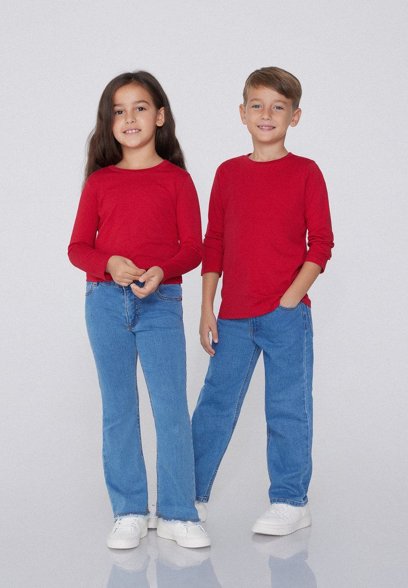 Rote Langarmshirts kombiniert mit blauen High-Waisted-Jeans. Die Kinder tragen weiße Turnschuhe. Einfaches Design, Baumwollmaterial und lässige Passform.