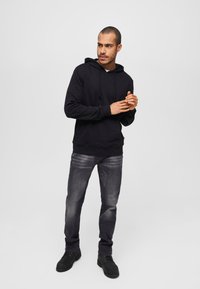 Must üleke mustast puuvillast, millel on nööbid, valge T-särgi peal, tumedate hallide teksade ja mustade nööbisaabastega. Sile tekstuur.