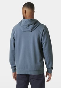 Sudadera con capucha azul que presenta un tejido texturizado, puños acanalados y un dobladillo recto. El diseño es sencillo con un corte relajado.