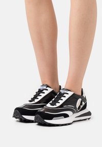 Baskets de sport en noir et blanc avec un mélange de cuir lisse et de daim. Dotées d'une semelle épaisse, d'un bout rond et d'un laçage à l'avant.