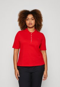 Camisa polo corta roja de manga corta con una botonadura y cuello, fabricada en una tela suave. Un pequeño logo es visible en la zona del pecho izquierdo.