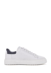 Zapatilla baja blanca con cordones blancos y suela gruesa, que cuenta con un cuello acolchado de talón azul oscuro, mostrada en perfil derecho.