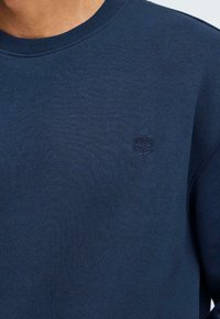 Kraljevo modra majica s kapuco iz teksturirane tkanine. Ima rebrast ovratnik in majhen embosiran logotip na prsih. Preprost, vsakdanji dizajn.