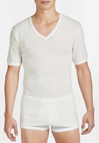 Maglietta bianca a maniche corte con scollo a V realizzata in tessuto morbido; presenta rifiniture a contrasto lungo lo scollo e le maniche. Il modello indossa pantaloncini bianchi.